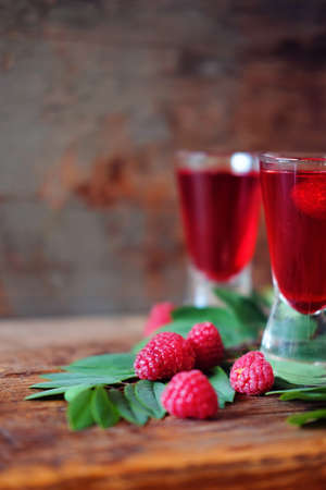 Raspberry fruit liqueur in two shot glasses with berries and green leaves. Strong local alcohol drinks.の写真素材