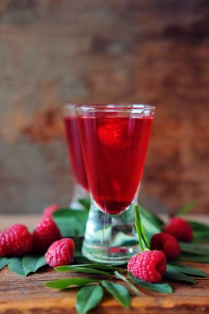 Raspberry fruit liqueur in two shot glasses with berries and green leaves. Strong local alcohol drinks.の写真素材