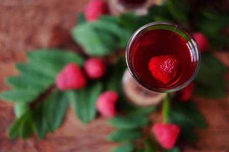 Raspberry fruit liqueur in two shot glasses with berries and green leaves. Strong local alcohol drinks.の写真素材