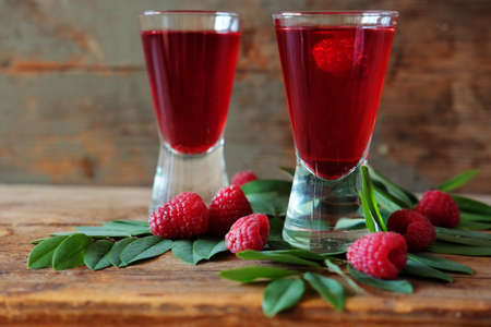 Raspberry fruit liqueur in two shot glasses with berries and green leaves. Strong local alcohol drinks.の写真素材