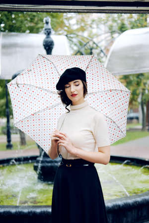 Young Parisian woman wearing black beret walking under the rain with dots umbrella. melancholic autumn mood.の写真素材