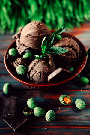 Three scoops of dark cacao ice cream sundae sprinkled with chocolate with mint leaves and spicy coated green peanutsの写真素材