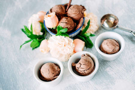 Three scoops of dark chocolate ice cream sundae with sweet floral flavour surrounded by roses,...
