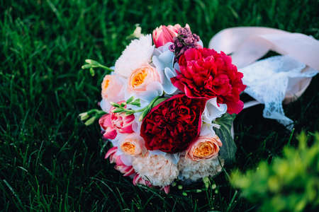 Bridal bouquet on green grass. Red and white peonies, freesia, roses and lilac flowers decorated with ribbons and laceの写真素材