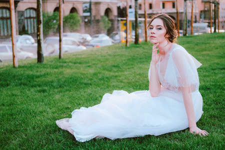 Charming young bride in white dress sitting on the lawn in the summer eveningの写真素材