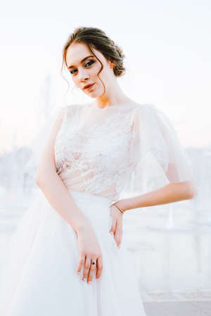 Happy young bride in flowing white dress enjoying herself outdoors and dancing near the fountain