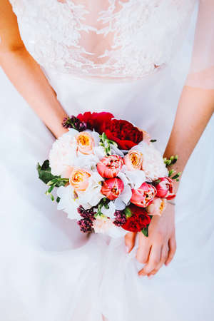 Adorable caucasian bride in white flowing wedding dress made of lace and tulle holding bridal bouquetの写真素材
