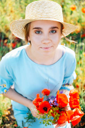 Cute blond young woman with braided hair in the field of red poppies and blue flowersの写真素材