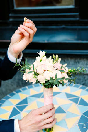 Handsome groom in dark blue suit holding engagement ring and bouquet and proposing to the bride
