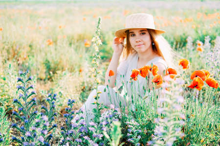 Young countryside girl with long blond hair in the field of poppiesの写真素材