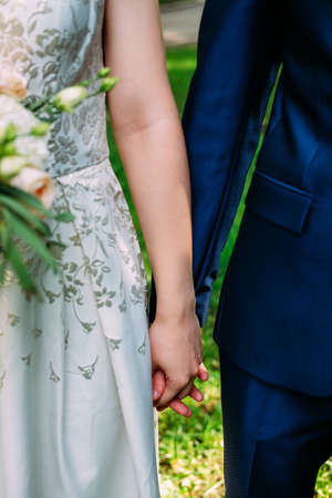 Husband and wife in blue suit and wedding dress getting married and holding handsの写真素材