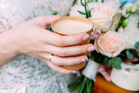 Young beautiful bride holding flowers and cup of coffeeの写真素材