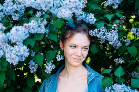 Smiling young adult woman hiding in lilac bushes