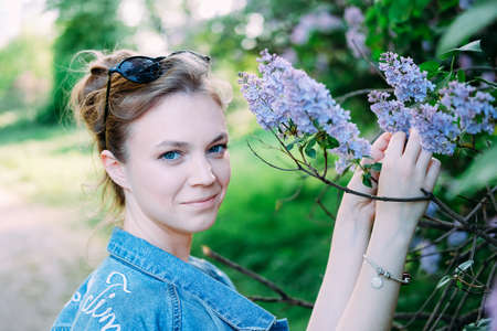 Smiling young adult woman hiding in lilac bushes