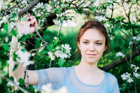 Calm and pretty young woman in the garden wearing transparent blue dress