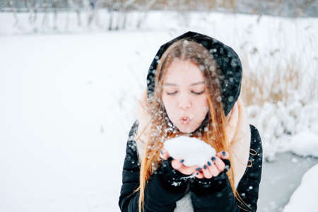 Attractive blond young adult woman having fun with the first snow wearing casual outfit of black parka, jeans, pink leather boots and backpack and beige shawlの写真素材