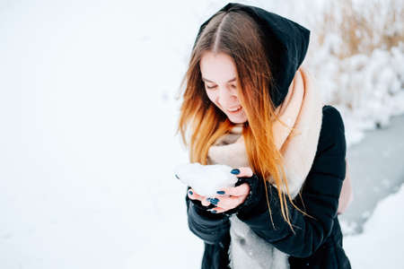 Attractive blond young adult woman having fun with the first snow wearing casual outfit of black parka, jeans, pink leather boots and backpack and beige shawlの写真素材