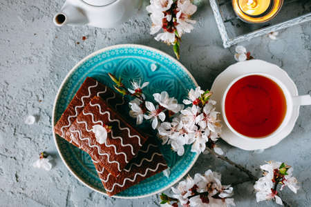 Sweet sunday dessert. Chocolate brownies with black tea on table decorated with flowers and candles.