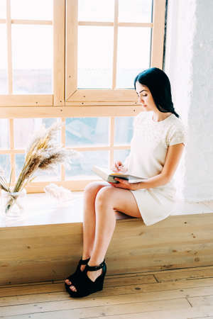 Young student woman with long black hair sitting in the class reading a bookの写真素材