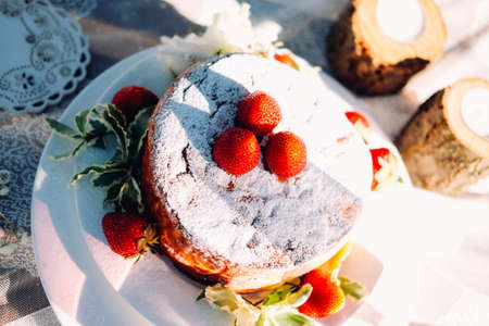 Strawberry cheesecake sprikled with sugar powder and decorated with berries and leaves. Table...