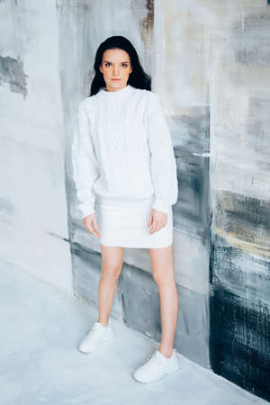 Brunette in white minimalist outfit. Winter knitted sweater.