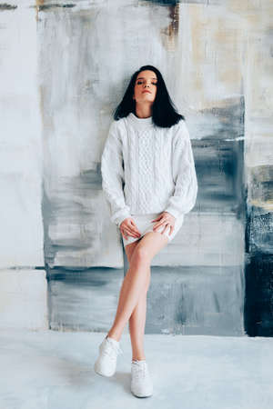 Brunette in white minimalist outfit. Winter knitted sweater.の写真素材