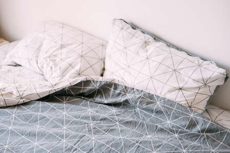 Gray and white unmade rumpled bed. Geometric bedsheets pattern.