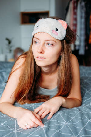 Happy young woman resting at home lying in the bed in her sleeping mask and pajamasの写真素材