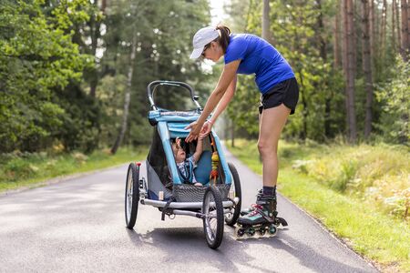 Young fit mother women skating outdoors with baby stroller