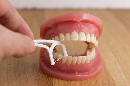 Man cleaning a pair of false teeth with dental floss demonstrating how to clean between the teeth over a wooden backgroundの写真素材