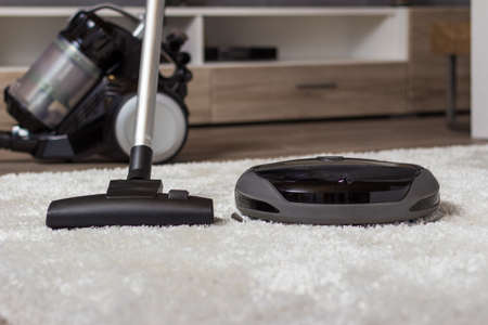 TraditiTraditional vacuum cleaner with a hose, nozzle and brush versus a modern circular automated low profile unit.onal vacuum cleaner versus a modern one