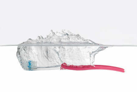 Colorful red toothbrush falling into clear clean water with a splash in a side viewの写真素材