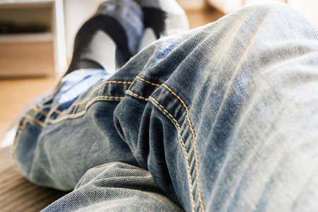 Close-up cropped view of crossing legs in blue jeans of person lying or sitting on parquet floor at home, feet in socks, shot from photographer point of viewの写真素材