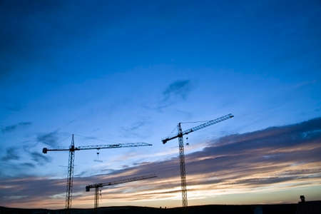 Several cranes abandoned at the sunset in a construction of buildings, Spain