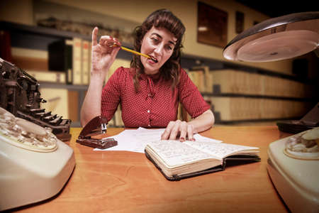 thoughtful clerk with a pencil in your mouth look at your agenda in office, 1960の写真素材