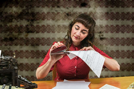 Young woman with red dress stapling papers in office, 1960の写真素材