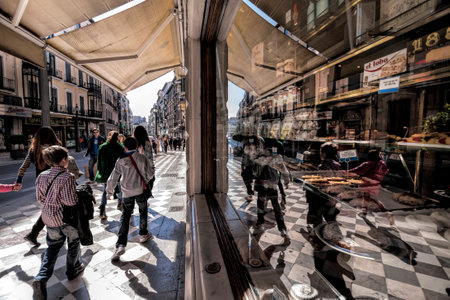 People walking on Reyes Catolicos street and reflected in the shopwindow of the old pastry Lopez...