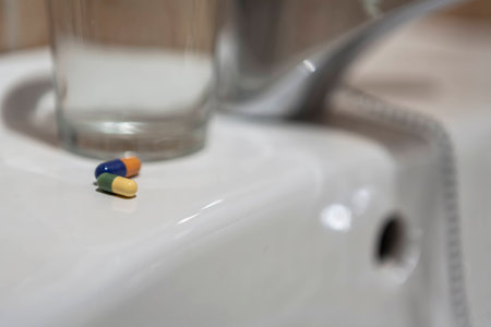 Glass of water and pile of blister packs in bathroom shelf