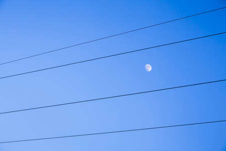 Moon between high voltage cables on bottom of the blue skyの写真素材