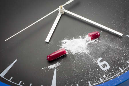 Open red capsule pill with white powder drug on black clock backgroundの写真素材