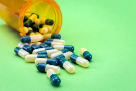 Pills spilling from an open bottle isolated on green backgroundの写真素材