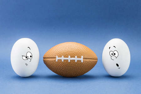 Two eggs look with strange face to a balloon of rugbyの写真素材