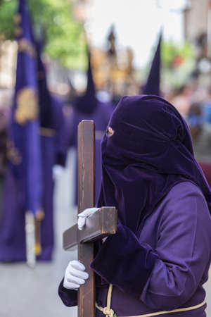 Penitent dressed in purple tunic of velvet resting on wooden cross during atonement station on Holy Week, Andalusia, Spainの写真素材