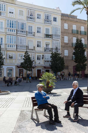 Elderly talk sitting on a bench with tranquility in a beautiful square of Cadiz, Andalusia, Spainのeditorial素材