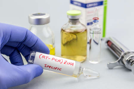 Scientist with blue latex gloves holds vials of ZIKA virus in laboratory for analysis