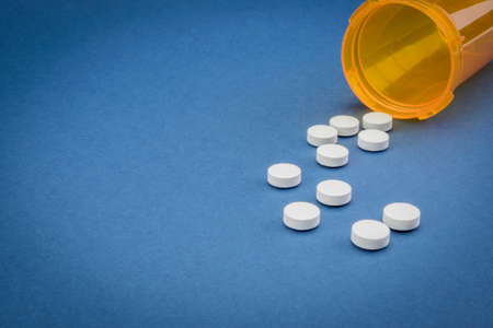 Pills spilling from an open bottle on blue backgroundの写真素材