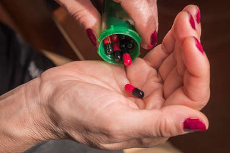 Women take red and black capsule with right hand from a green bottle on black backgroundの写真素材