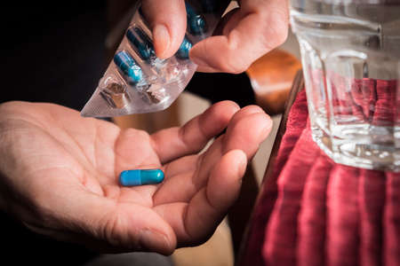 Women take blue capsule with left hand from a container pills