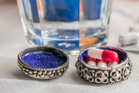Metallic pillbox with white and red capsules along with water glass