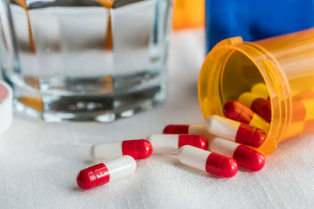 Red and white pills, glass water transparent along